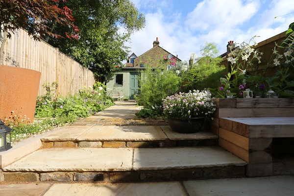 2 Mint sandstone steps with rock-faced edge profile on brick risers ascend to straight path to shed at bottom of garden.