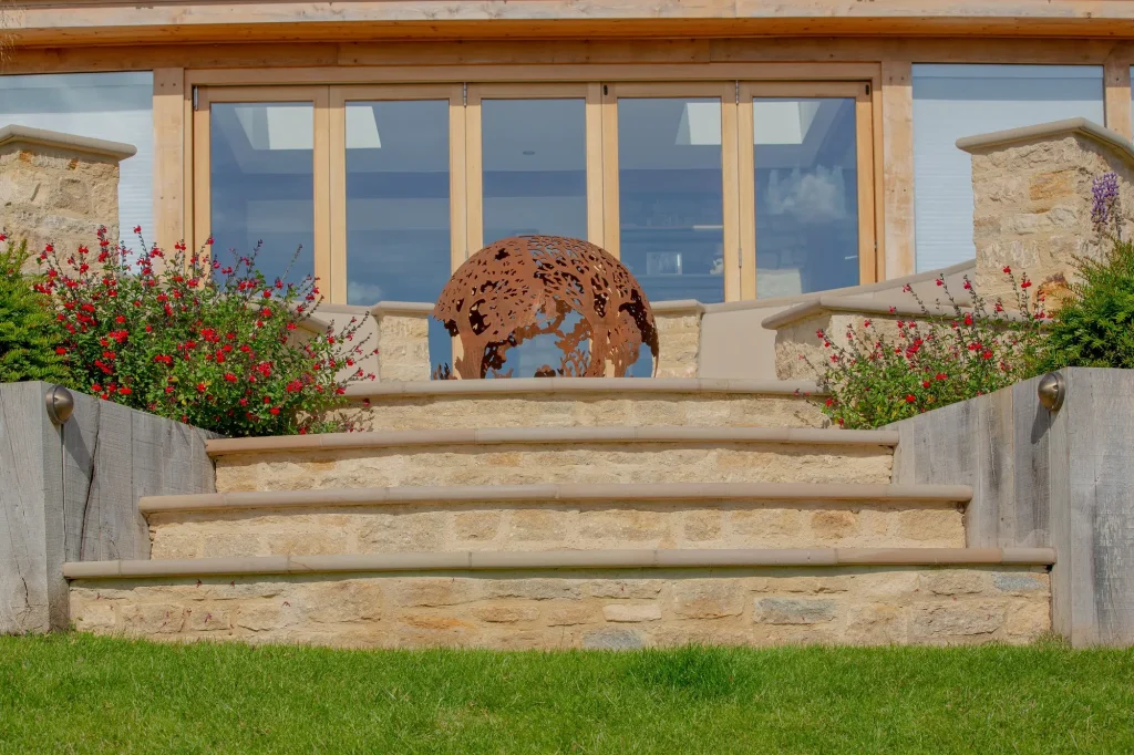 Curved buff sandstone bullnose steps rise between flanking walls to pierced iron fire ball in front of patio doors.