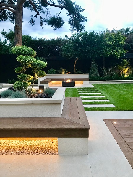 Golden Stone porcelain 40mm downstand coping on raised bed with wooden bench on all 4 sides. Lawn with slab stepping stones beyond.