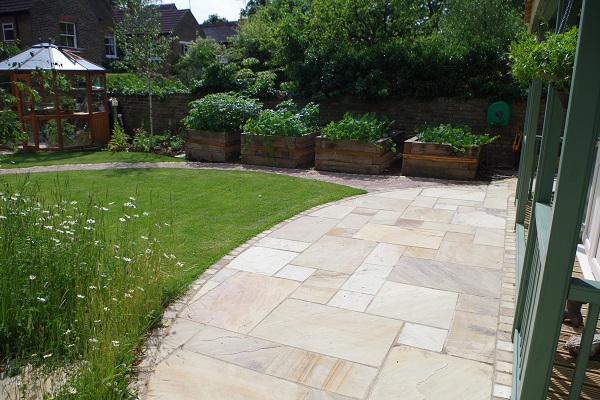 Half moon-shaped Mint Indian sandstone patio idea, edged with setts, next to lawn.