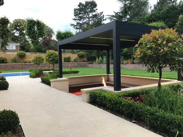 Sunken seating area edged with Gold Stone porcelain coping, under pergola. Lawn beyond.