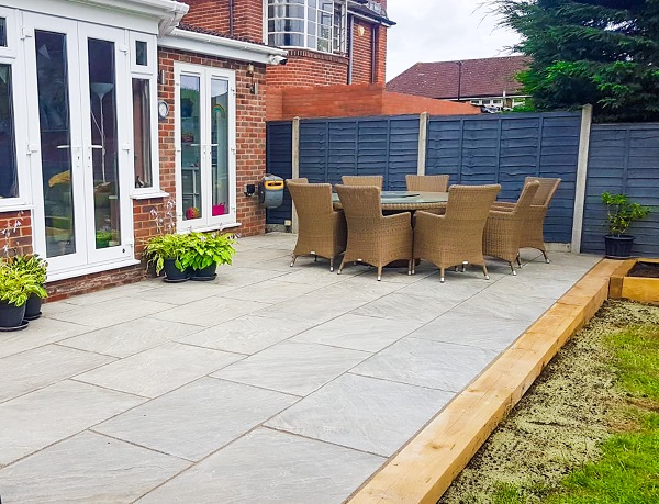 Kandla Grey Indian sandstone patio with straight timber sleeper edge, outside french doors of brick house.