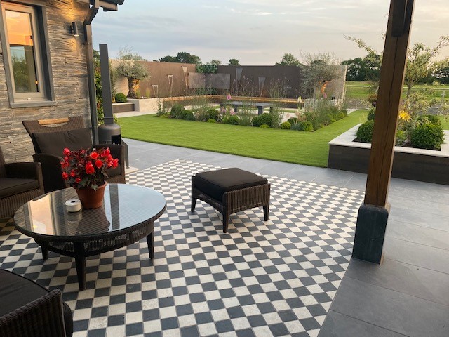 Cream and Charcoal porcelain setts laid in chequerboard pattern to define seating area under pergola with view of garden.