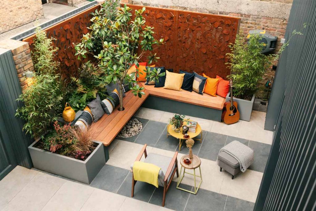 View down onto small town garden with two-tone patio. Inbuilt bench seating sits between planters against tall clad wall.