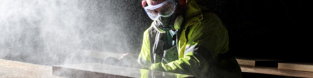 Man in protective breathing equipment and hi-vis jacket polishing edge of natural stone slab.