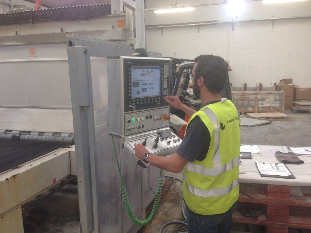 Man in hi-vis jacket stands at screen of CNC cutting machine.