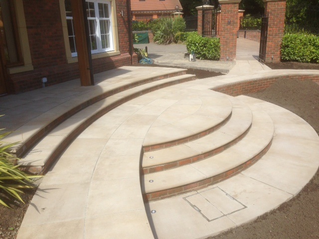 Curved steps meet an oppositely curved patio with 2 steps rising across width of house. 