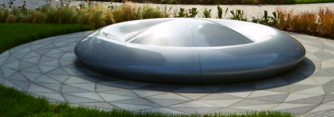 Circular sculpture sits on circle of bespoke paving of granite and basalt cutinot triangles.