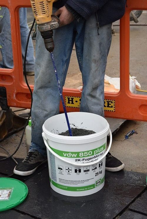 Mixing hardener into brush-in patio grout with drill.