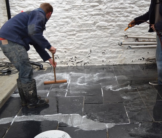 2 men brush GftK mortar into paving joints, one holding a hose.