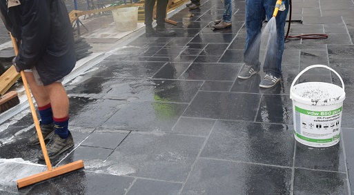 Feet of people standing on sandstone paving, washing off mortar residue. 