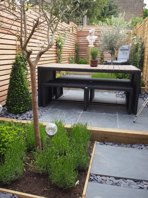 Black slate paving and chippings with slatted wood fende and bench table.