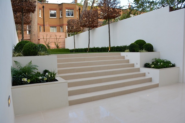 Oblique view of 8 Warm Beige porcelain steps rising between raised beds to artificial lawn between rendered garden walls.