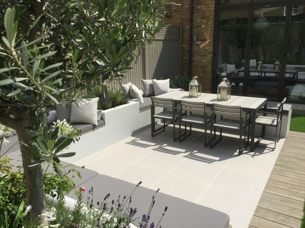 Urban grey porcelain patio with outdoor dining set, grey cushioned benches around edge. Design by Harrington Porter.