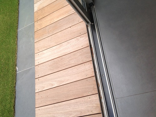 Close view of sliding door opening showing matching indoor and outdoor tiles separated by  Iroko decking.