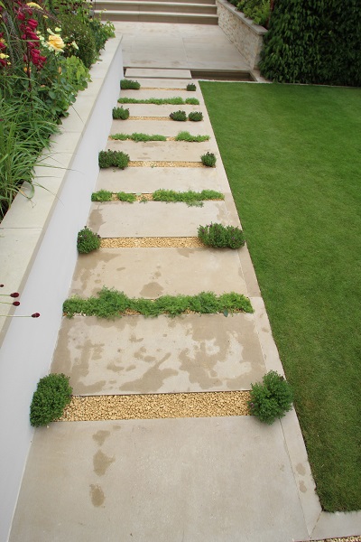 Darleymoor Buff Yorkstone paving stones laid with wide joints between wall and lawn.