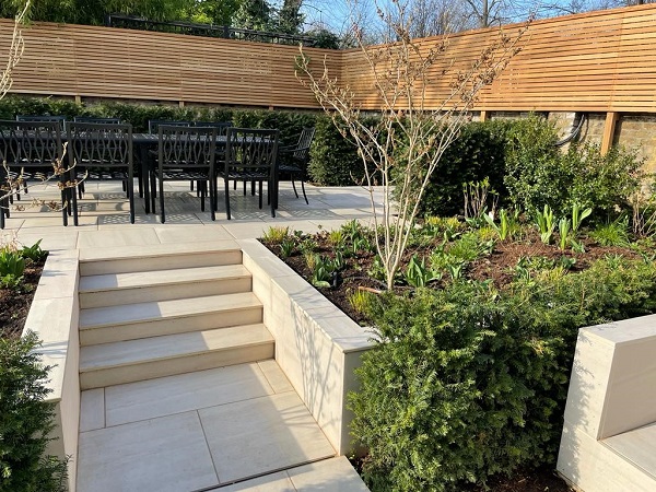 Faro porcealain steps rise to patio between 2 long flanking walls supporting raised beds.