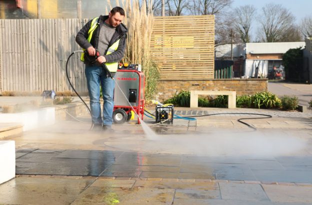 Man showing how to clean porcelain outdoor tiles with a jet wash held at the right angle and with correct power setting