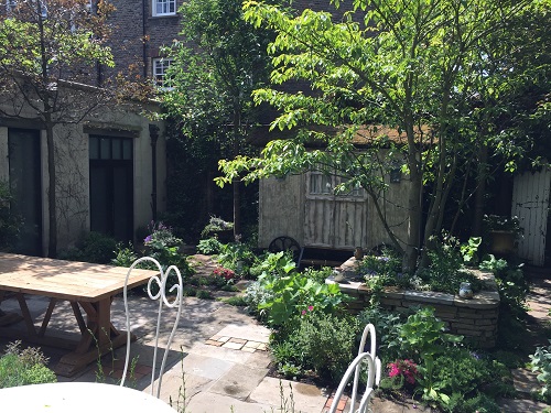 An old wooden table, reclaimed paving and a fence with pretend doors create a secret gardens feel.