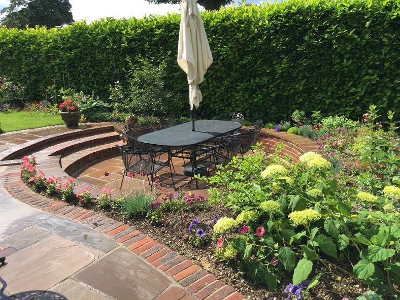 Autumn Brown sandstone patio with round sunken dining area, shrubs and hedge.