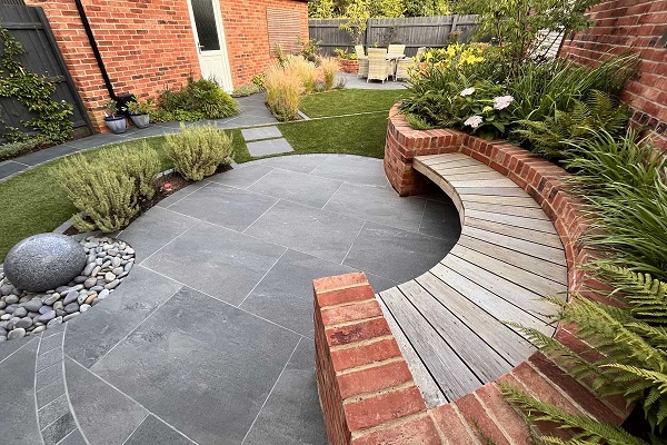 Oval patio of Platinum Grey porcelain paving, with pebble water feature and slatted bench.Design by Mark Langford. 