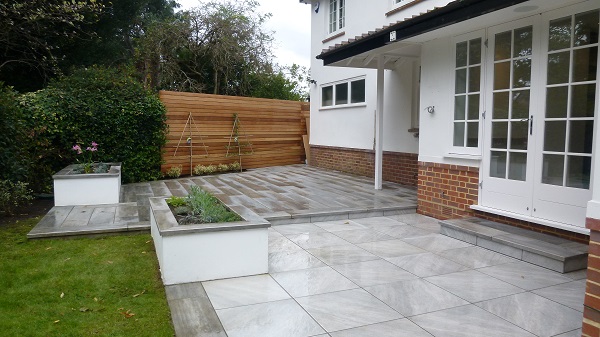 2 tone patio of Cinder and light grey porcelain paving with rectangular planter at back of white painted house. 