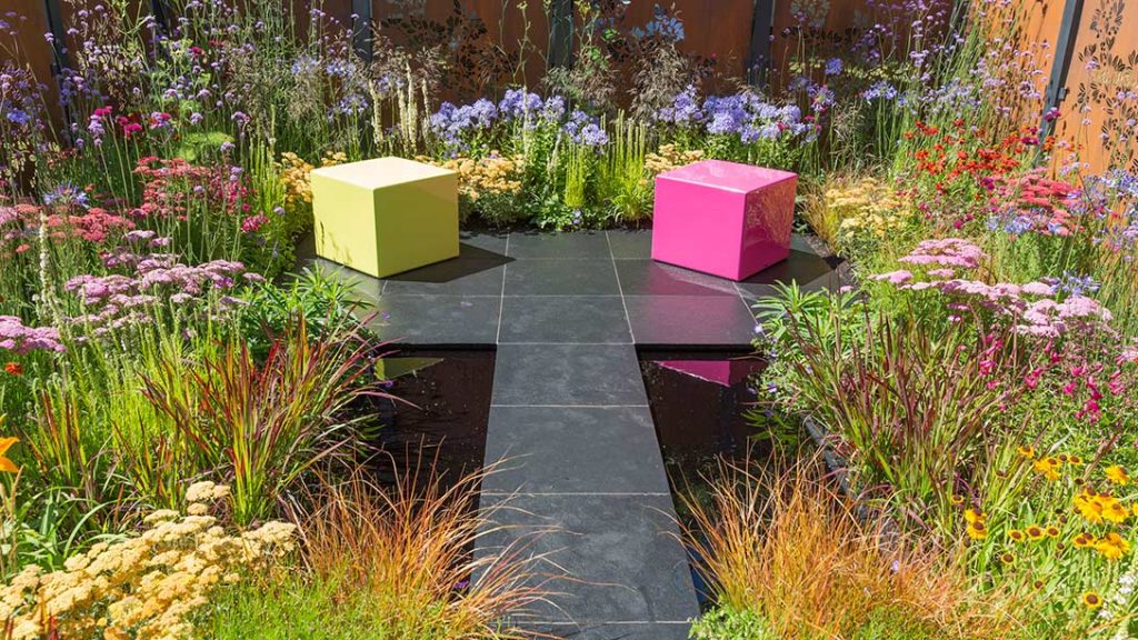 Natural stone patio idea of 2 coloured cubes on T-shaped paving of Midnight Black limestone, surrounded by bright planting.