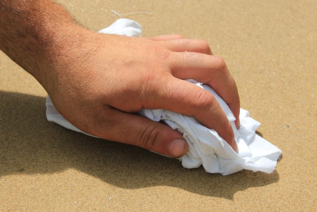 Close-up of hand holding white cloth, rubbing dry the surface of sealed sandstone paving.