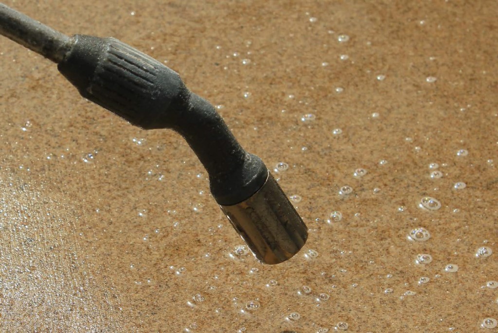 Low pressure nozzle close to surface of paving slab, delivering sealing solution to sawn sandstone.