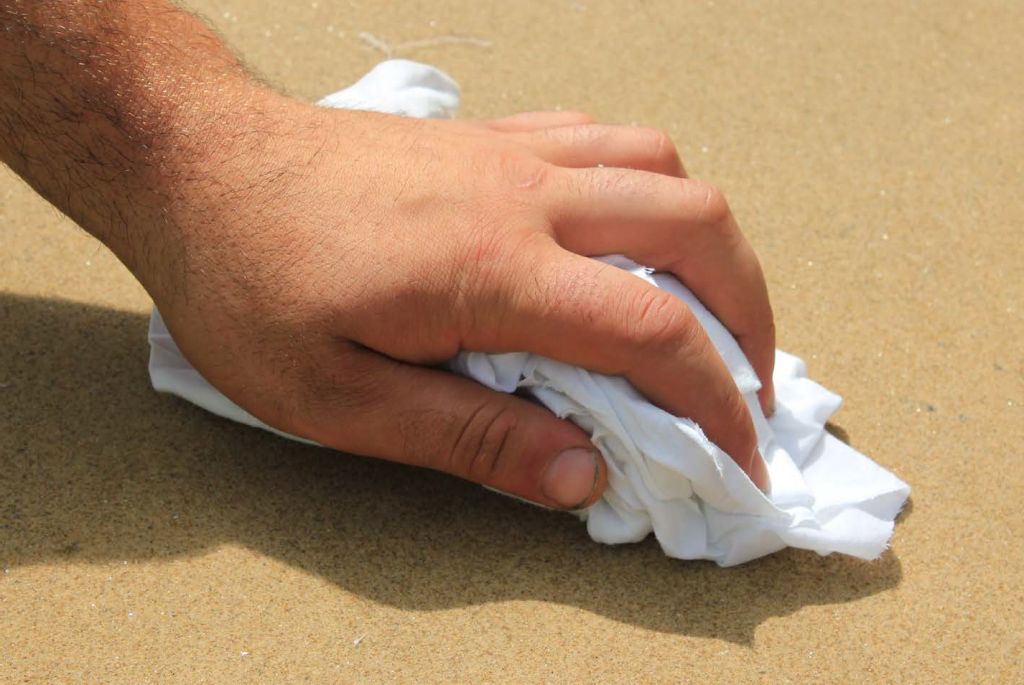 Close-up of hand holding white cloth, rubbing dry the surface of sealed paving. London Stone