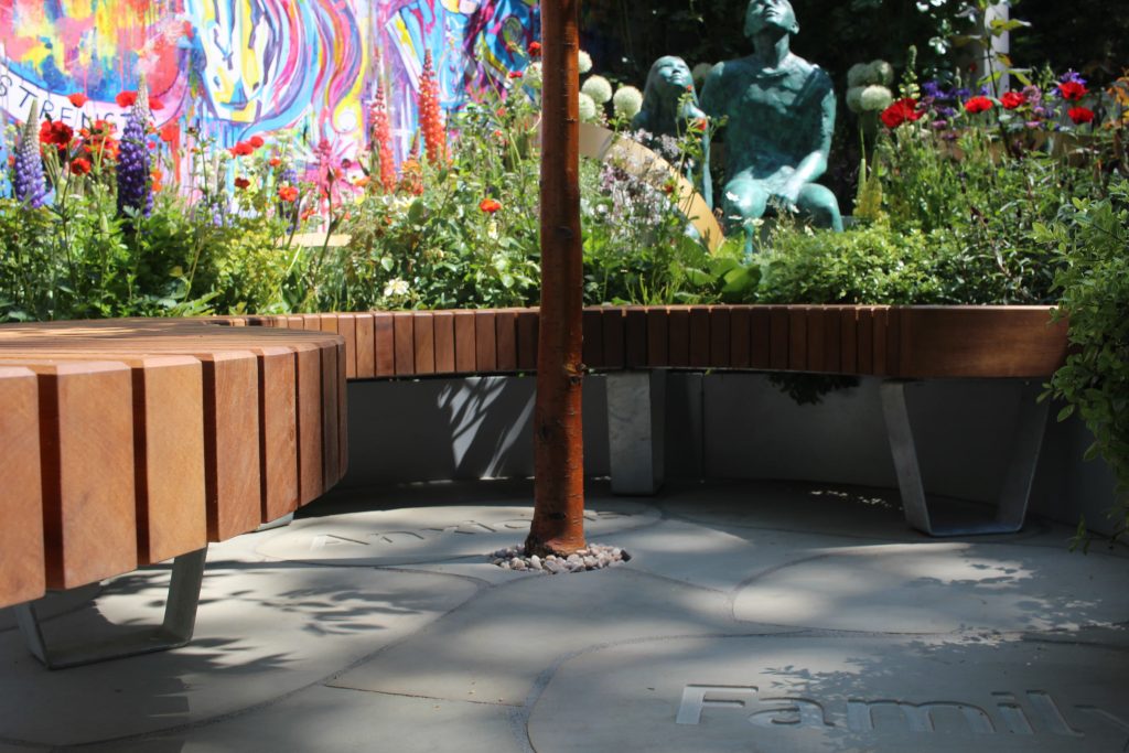 Figurative sculpture at back of raised bed edged by wooden bench over bespoke Heath sawn sandstone paving.