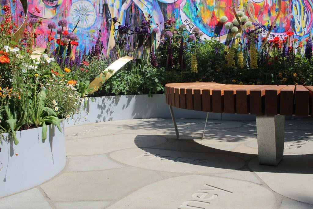Sinuous, multi-coloured wall and raised bed edges curve-cut Heath sawn sandstone paving, some slabs engraved with a word, in show garden RHS Chelsea 2018.