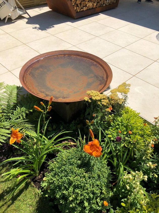 Corten Steel water bowl in planted border next to Slab Khaki porcelain paving