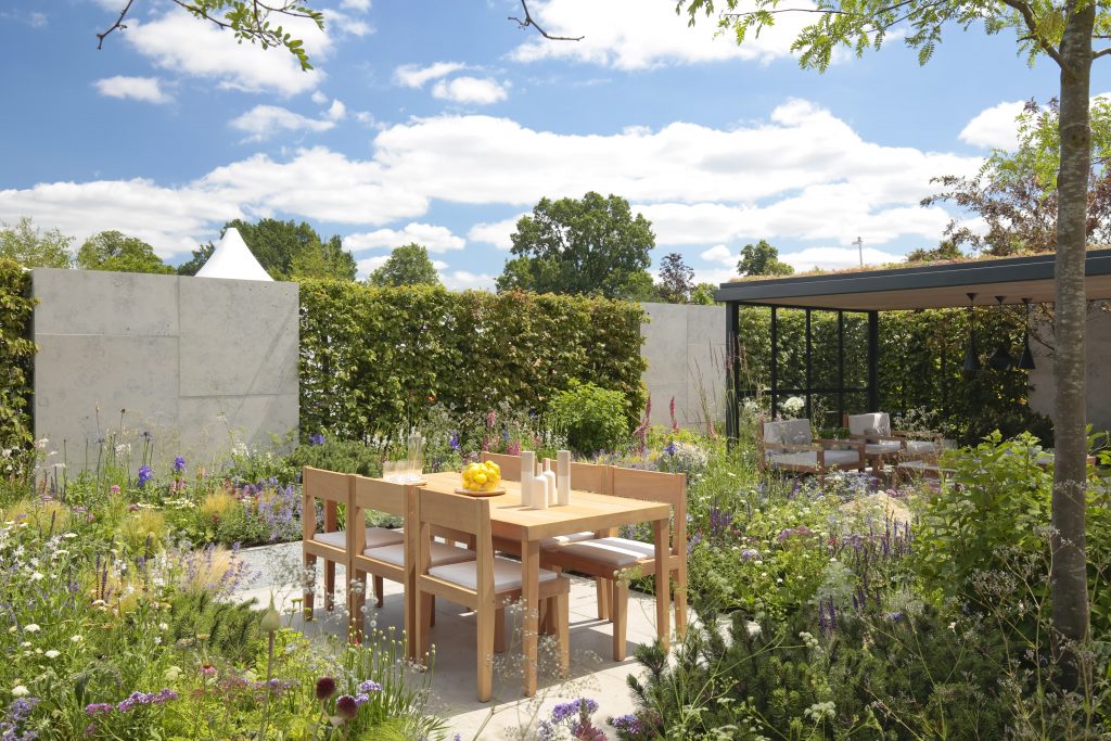 Hedging is paired with stone walling to soundproof this peaceful garden with wooden seating and plenty of planting. 