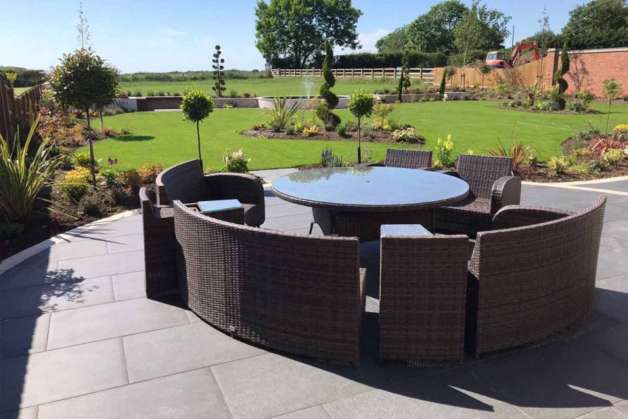 Round table and lounge set sits on round porcelain of Basalt Porcelain 600x900 outdoor tiles with lawn beyond.