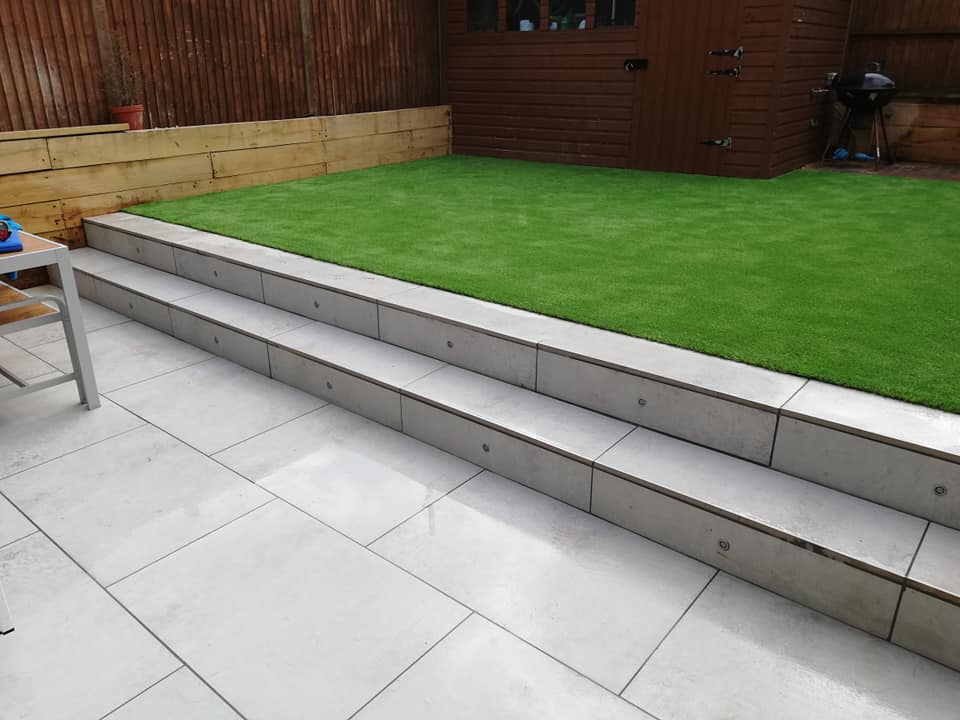 900x600 Light Grey porcelain patio slabs as paving and 2 wide steps up to lawn. Laid by Dorking Paving and Landscapes.