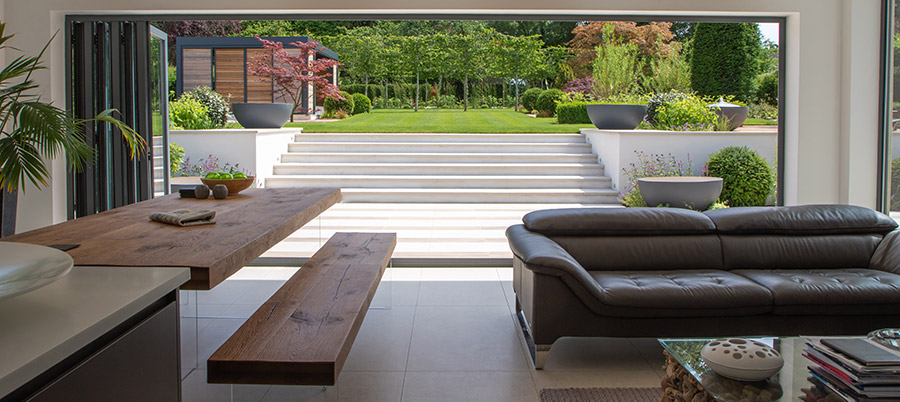 Patio and wide steps of Faro porcelain steps seen from inside house through open bifold doors. Built by PC Landscapes.