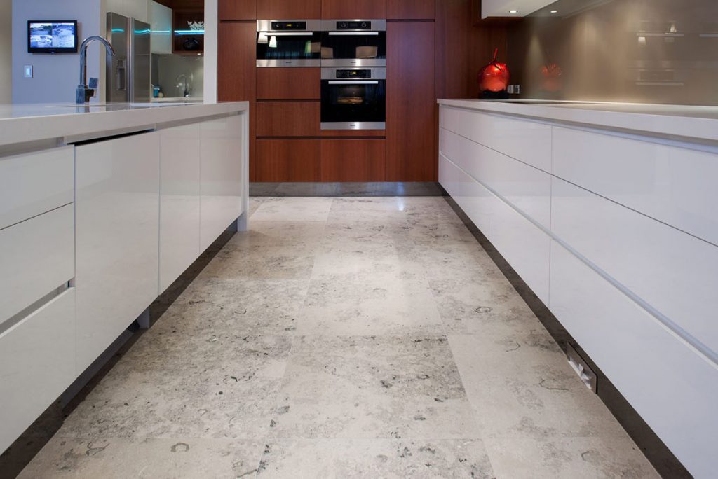 Jura Grey limestone wall and floor tiles used in kitchen between 2 rows of cabinets.