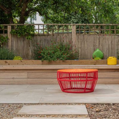Round orange seta on Cream porcelain paving with raised bed behind.