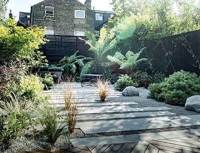 Beige sandstone plank paving laid in wide path with gravel in fenced garden with dry planting