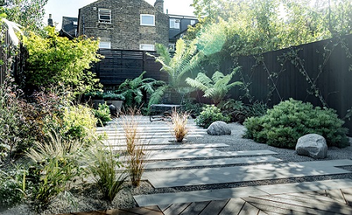 Beige sandstone plank paving laid in wide path with gravel in fenced garden with dry planting