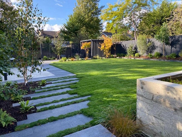 Black granite planks set into grass, leading to paved area in large garden. Design by Emelie Bausager.