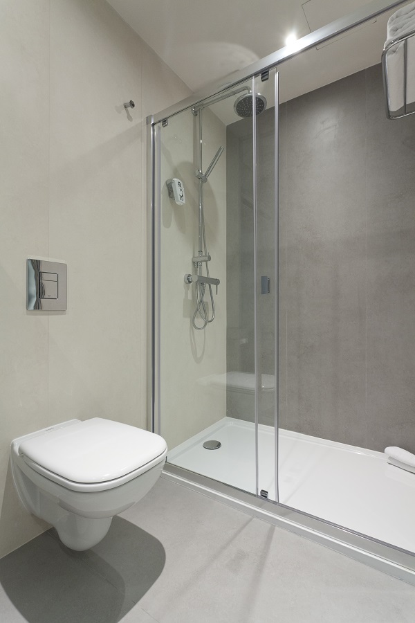 Closed toilet in front of glass sliding doors of shower with Hydra Argen porcelain clad wall.