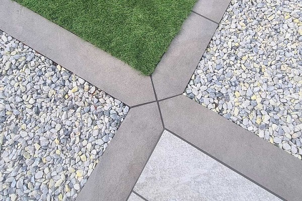 4 Steel grey porcelain planks meet with mitred joints, separating 4 areas of gravel, lawn and paving.