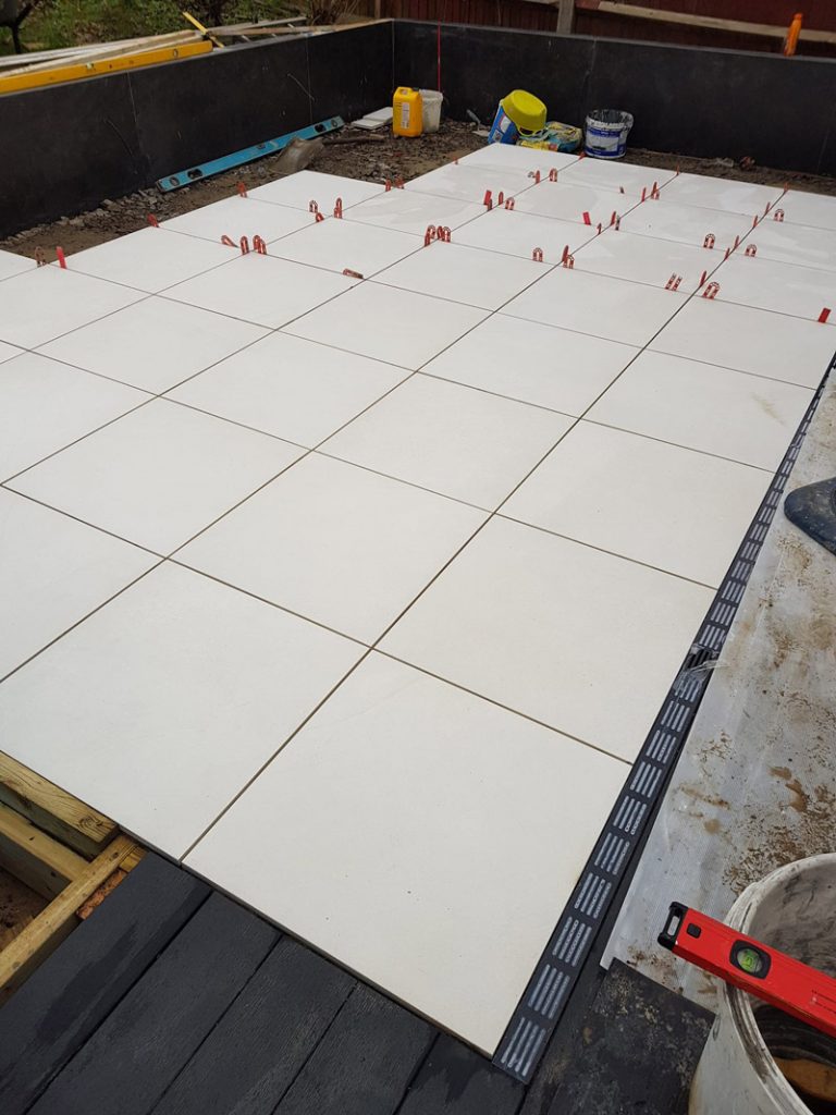 Comblanchien paving mid installation, show how to lay porcelain slabs with spacers in a stack bond pattern.