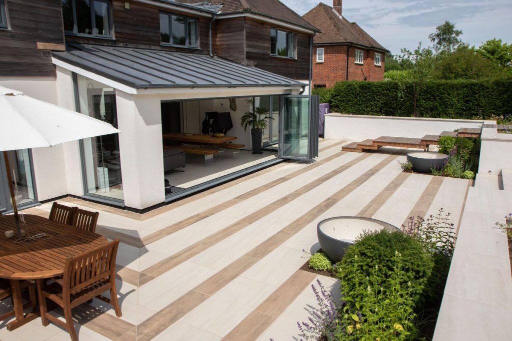 Wood-effect and plain porcelain tiles in stripes on patio across back of house. 