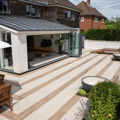 Wood-effect and plain porcelain tiles in stripes on patio across back of house.