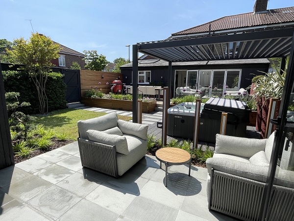 Large patio in back garden with louvred metal pergola over hot tub. Lawn beyond. 
