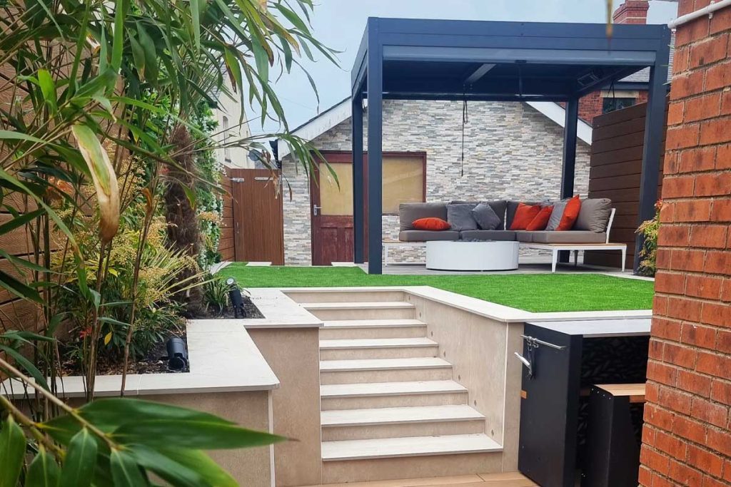 Steps rise to lawn with Dark Grey aluminium pergola with sides over patio and sofa