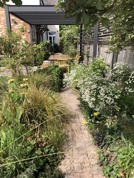 Path down side of garden between beds to grey aluminium pergola over garden furniture